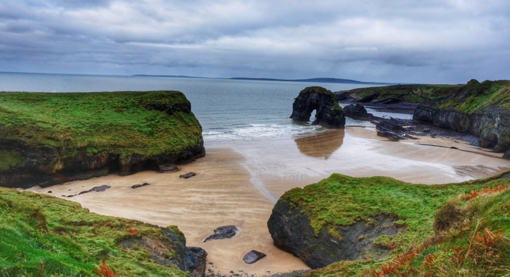 A scenic view of Ballybunion Beach with rugged cliffs and crashing waves.