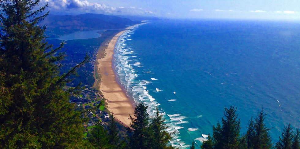 A scenic view of Manzanita Beach with waves crashing against the shore and Neahkahnie Mountain in the background.