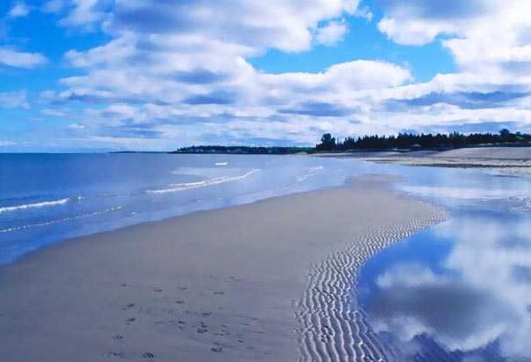 Sandy shoreline with calm waves and blue sky at Parlee Beach. 